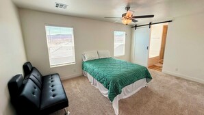 A bedroom with a bed, a black couch, two windows, a ceiling fan, and a door leading to another room. - Spacious 4BR in Red Trails 30+ Day Stays (Washington)