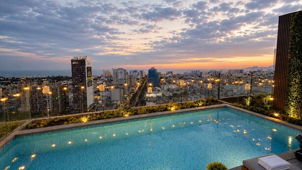 A rooftop pool with a cityscape view, lounge chairs, and string lights.