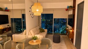 A modern living room with a glass dining table, a sofa, and a hanging light fixture.