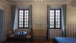 A room with two windows, a radiator, a table with chairs, and a bed. - Immerse yourself in this spacious 26m² room inspired by the mastery of light. (Giverny)