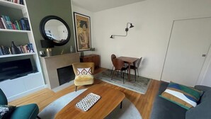 Una sala de estar con sofá, sillón, mesa de centro, chimenea, mesa de comedor, sillas, estantería y una lámpara de pared.