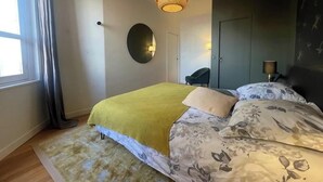 Un dormitorio con cama, espejo redondo, lámpara colgante, silla y armario.