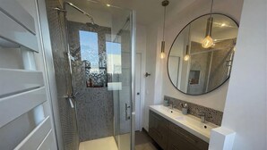 Un baño moderno con ducha de vidrio, un espejo redondo y un tocador blanco con lavamanos.