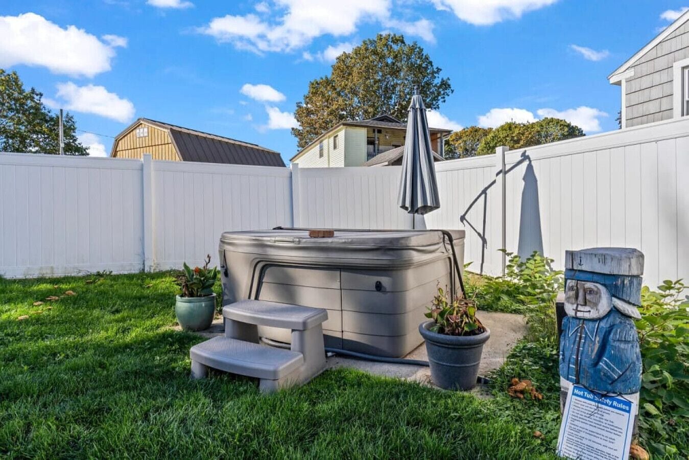 Un jacuzzi en un patio trasero con valla blanca, una sombrilla y una estatua.