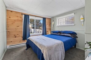 A bedroom with a bed, a window with curtains, a wall-mounted lamp, and a plant.