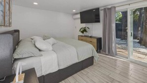Un dormitorio con cama, mesita de noche, televisión y puerta corrediza al balcón.