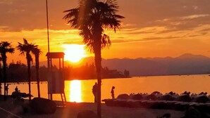 A sunset over a body of water with palm trees and a lifeguard tower. - At Lake Garda in the greenery and tranquility. (Veneto)
