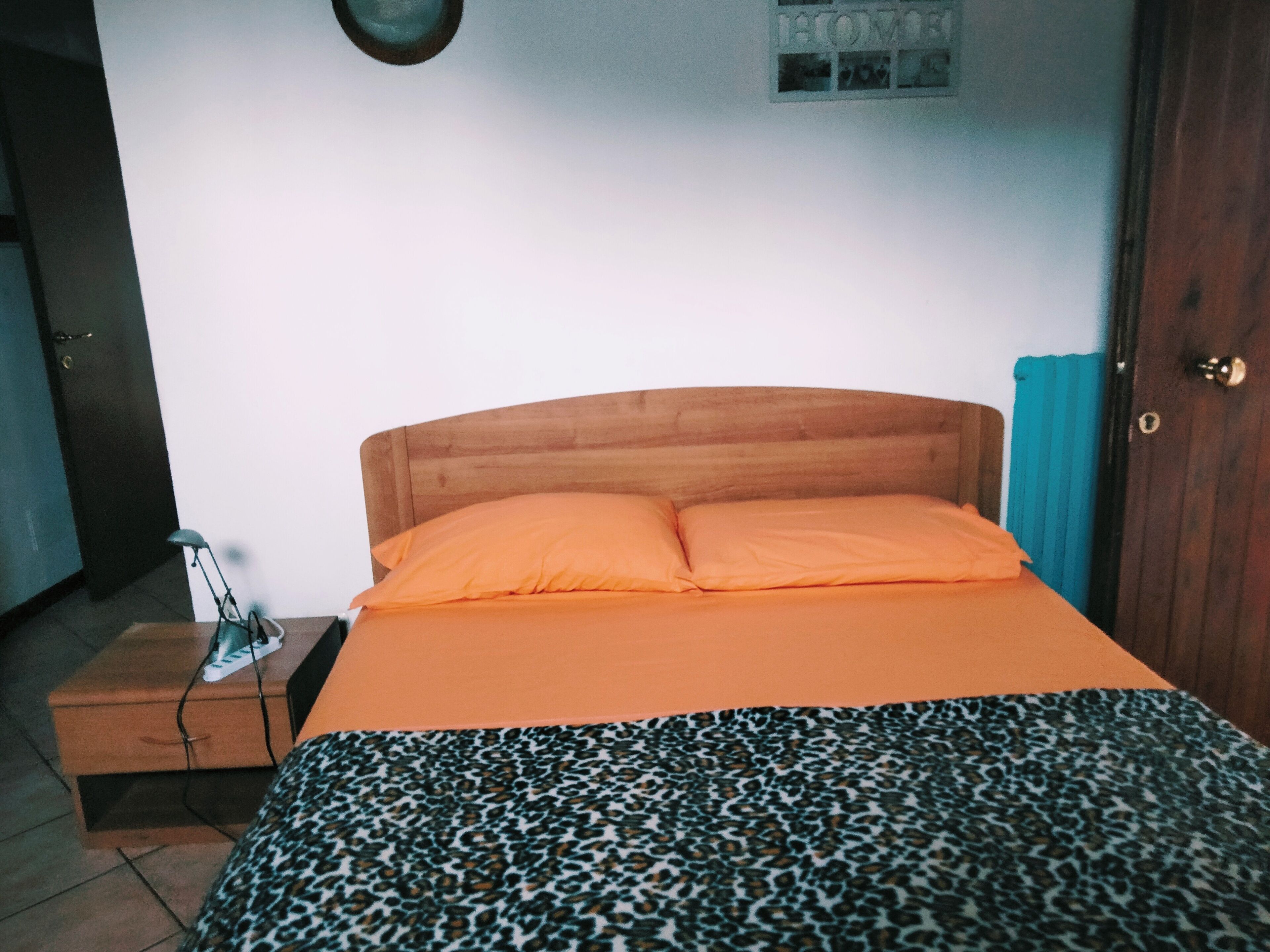 Ein Schlafzimmer mit einem hölzernen Bett, einer orangefarbenen Bettdecke, einer Decke mit Leopardenmuster, einem Nachttisch mit Lampe und einer Tür mit blauer Vorhang.