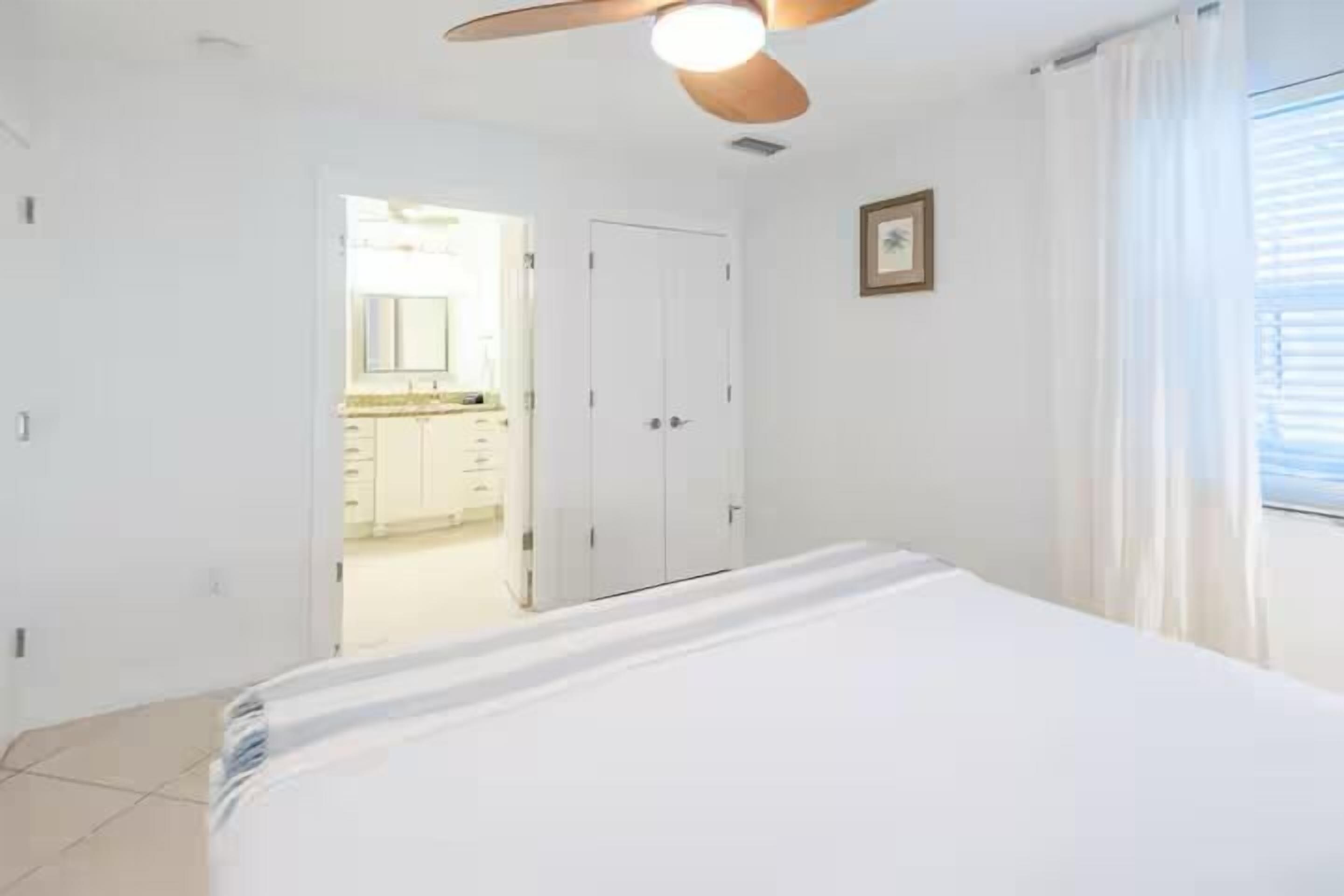 A bedroom with a bed, a ceiling fan, a door, and a window with curtains.