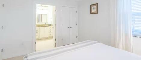 A bedroom with a bed, a ceiling fan, a door, and a window with curtains.