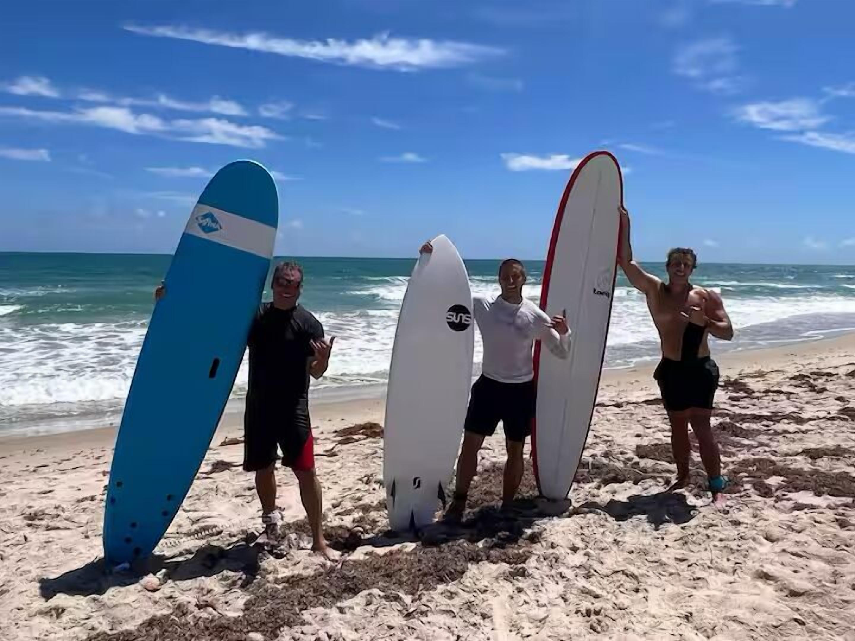 Quatre personnes tenant des planches de surf sur une plage, avec l’océan en arrière-plan.
