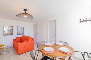 Ein modernes Wohnzimmer mit Esstisch für vier Personen, einer Couch und einer Deckenleuchte.