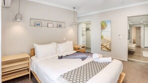 Una camera da letto con un letto, comodini, una ventola a soffitto e un corridoio che porta al bagno.