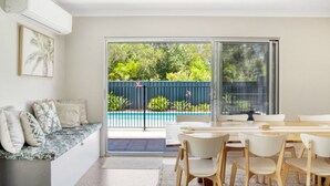 Un soggiorno moderno con vista piscina, un'area pranzo con sedie e un divano con cuscini.