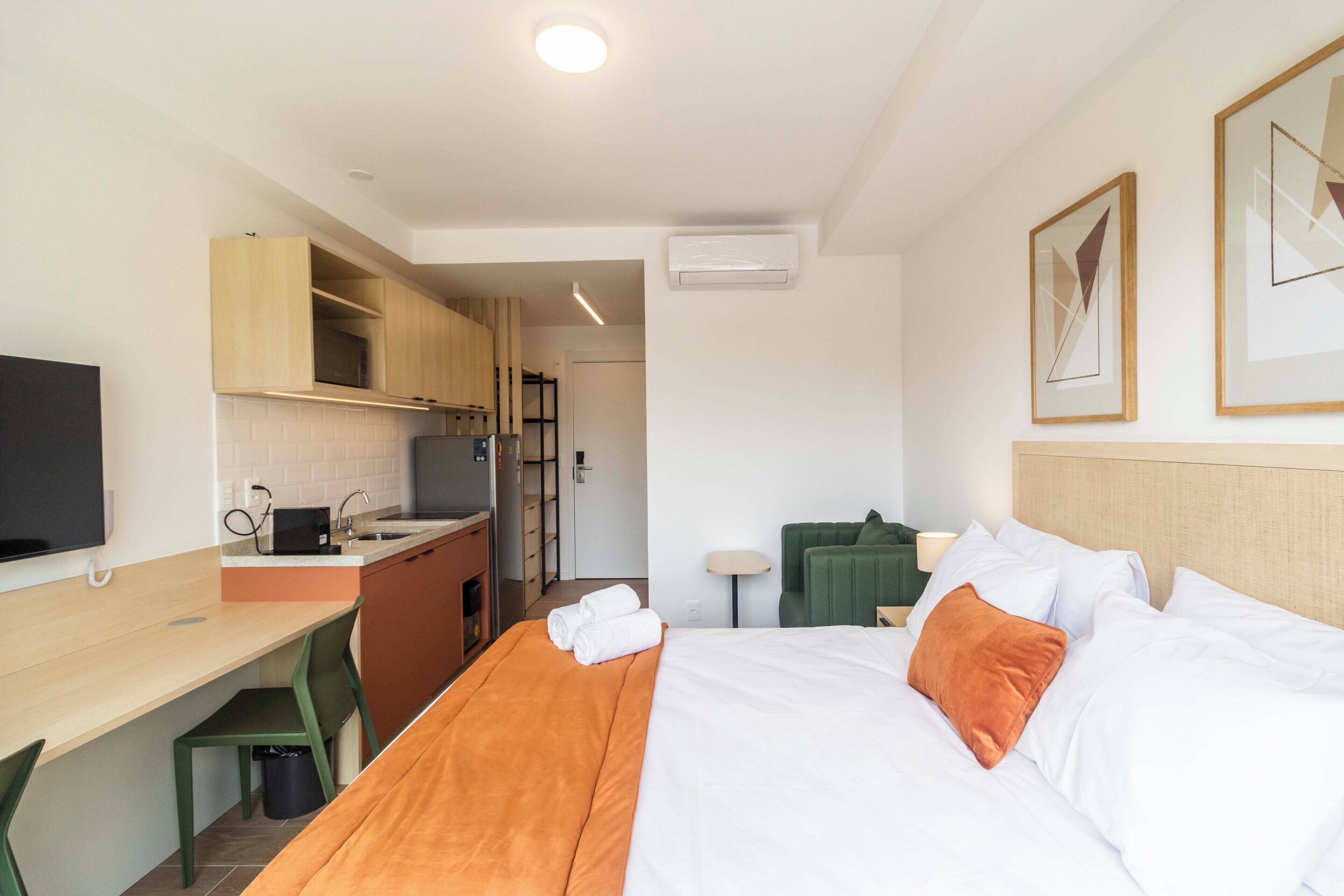 Hotellihuone, jossa on sänky, työpöytä, tuoli, televisio ja pieni keittiö.