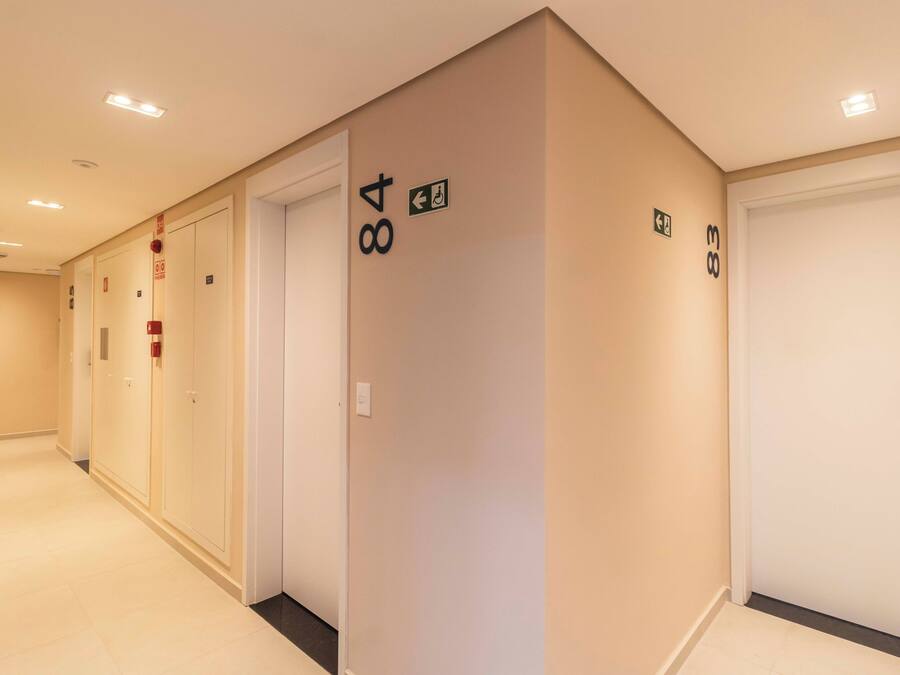 Een hotelgang met genummerde deuren, borden voor de vluchtweg en een brandmelder.