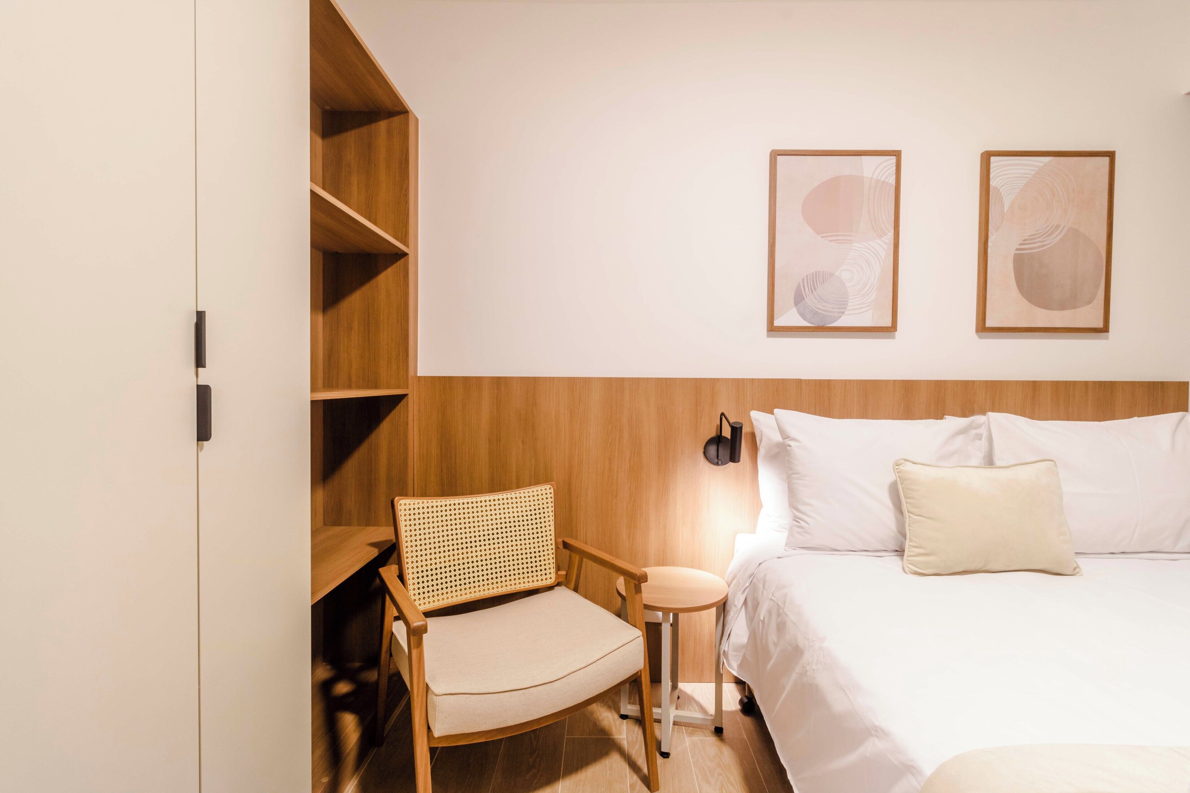 A hotel room with a bed, a chair, a small table, and two wall-mounted light fixtures.