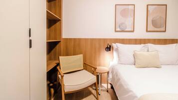Une chambre d’hôtel comprenant un lit, une chaise, une petite table et deux lampes fixées au mur.