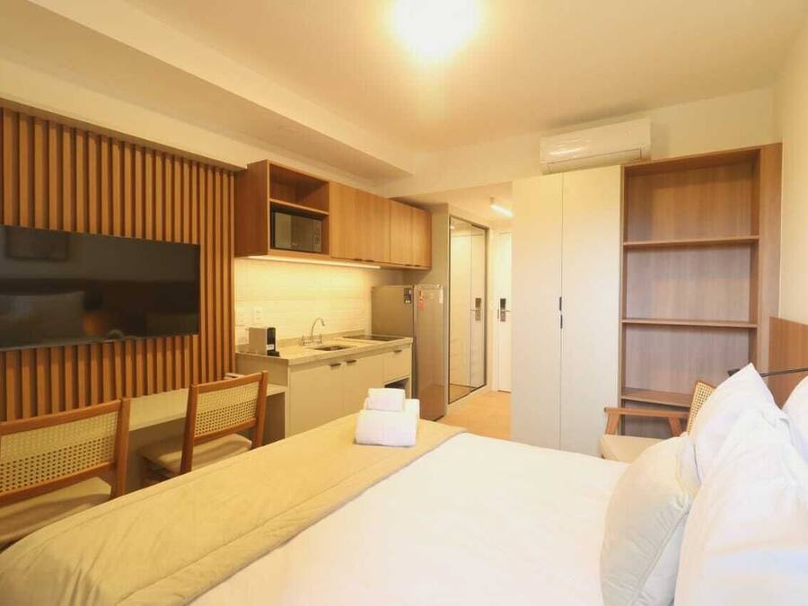 A hotel room with a bed, a TV, a kitchenette, and a bathroom.