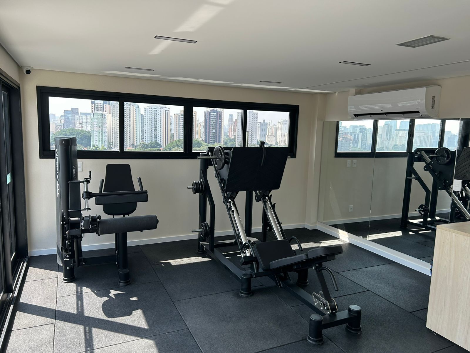 Une salle de sport équipée de matériel d’exercice, dotée de grandes fenêtres et offrant une vue sur la ville.