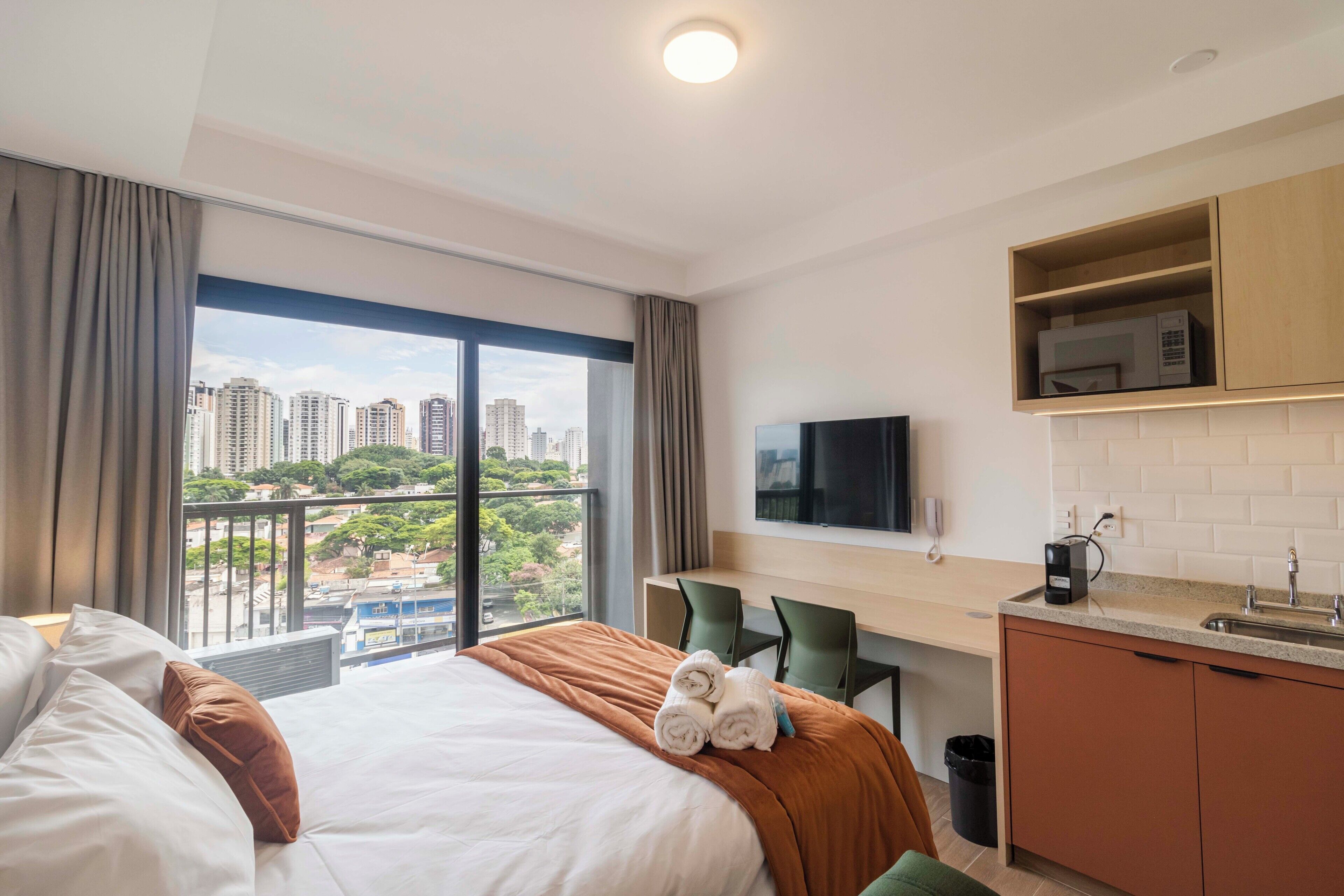 Habitación de hotel con cama, escritorio, televisor y vistas a la ciudad.