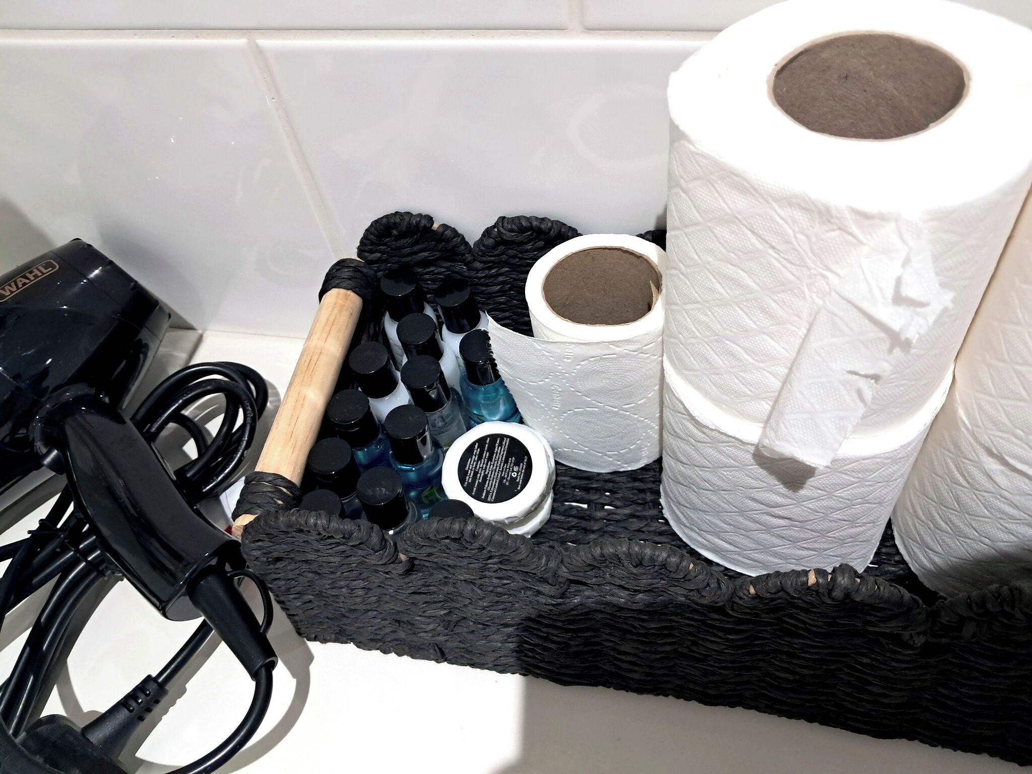 A bathroom with a black bath mat, a hairdryer, and a bottle of shampoo.
