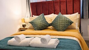 A bed with a red headboard, two green pillows, and three rolled towels. - 2 Bed Home - Parking, Private Garden, Wifi (Derby)