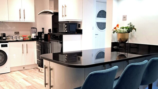 A modern kitchen with a central island, bar stools, and a washing machine. - 2 Bed Home - Parking, Private Garden, Wifi (Derby)