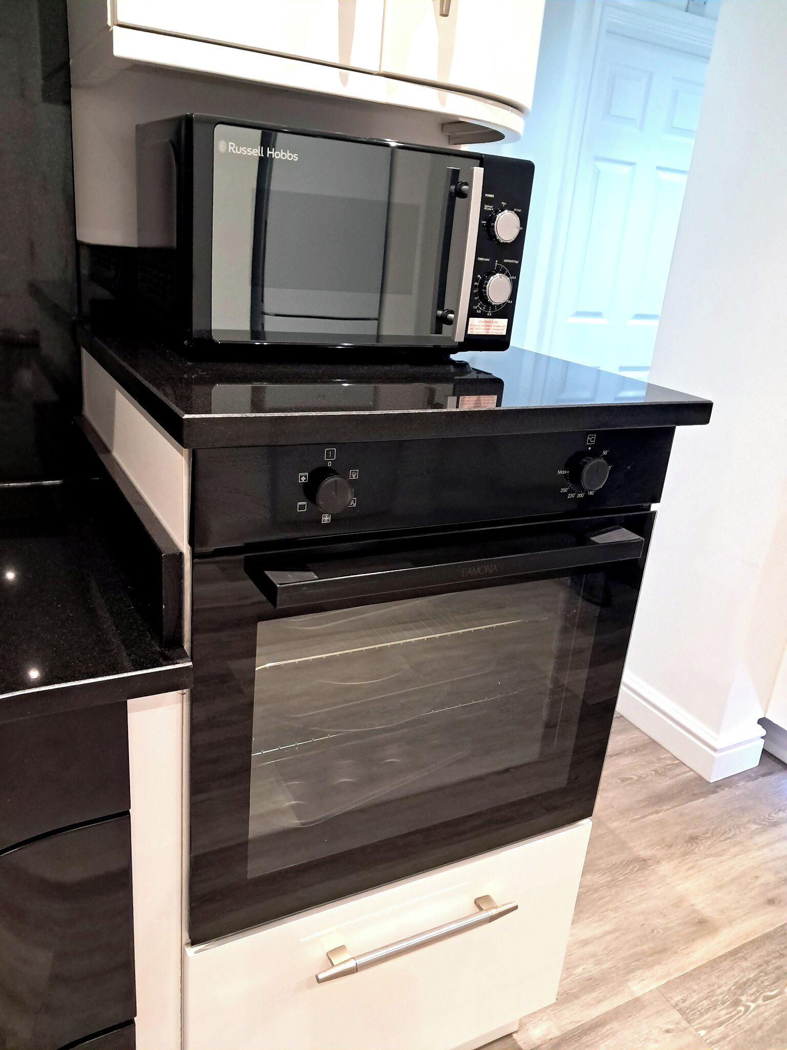 A kitchen with a microwave, oven, and a white cabinet above the oven.