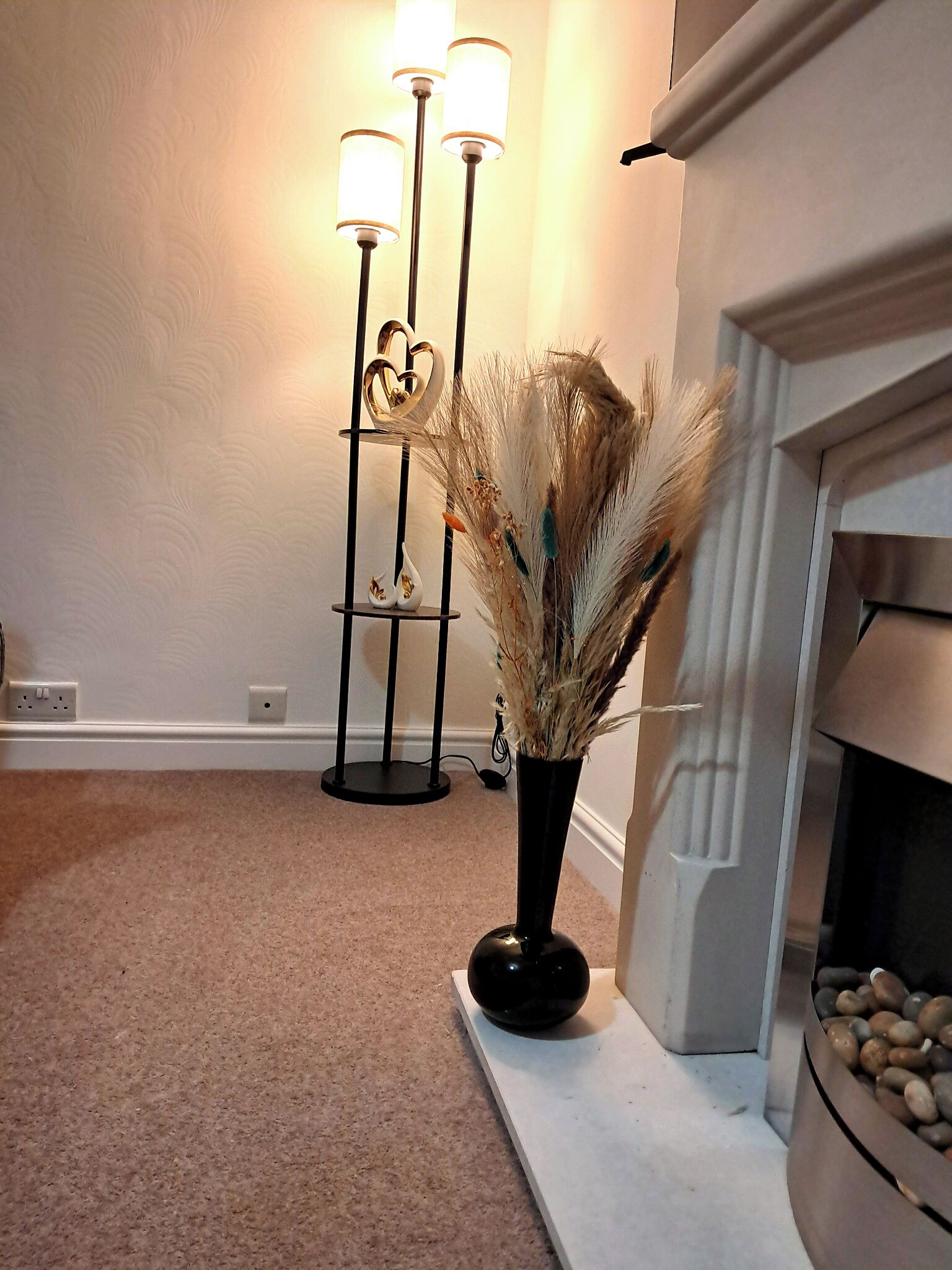 A room with a fireplace, a vase with dried plants, and a floor lamp.