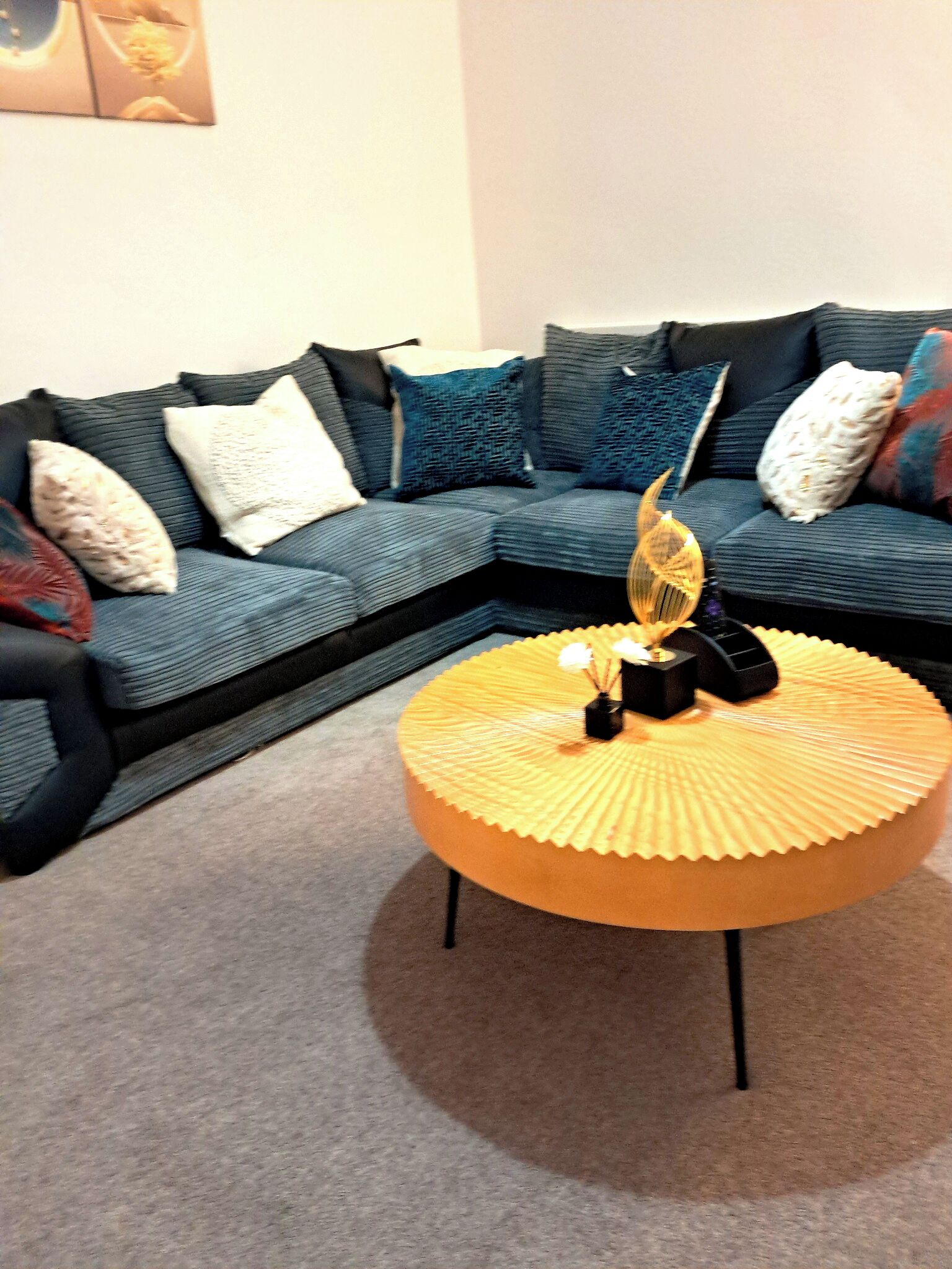 Ein Wohnzimmer mit einem dunkelblauen Sofa, mehreren Kissen und einem runden, gelben Couchtisch mit einem dekorativen Gegenstand darauf.