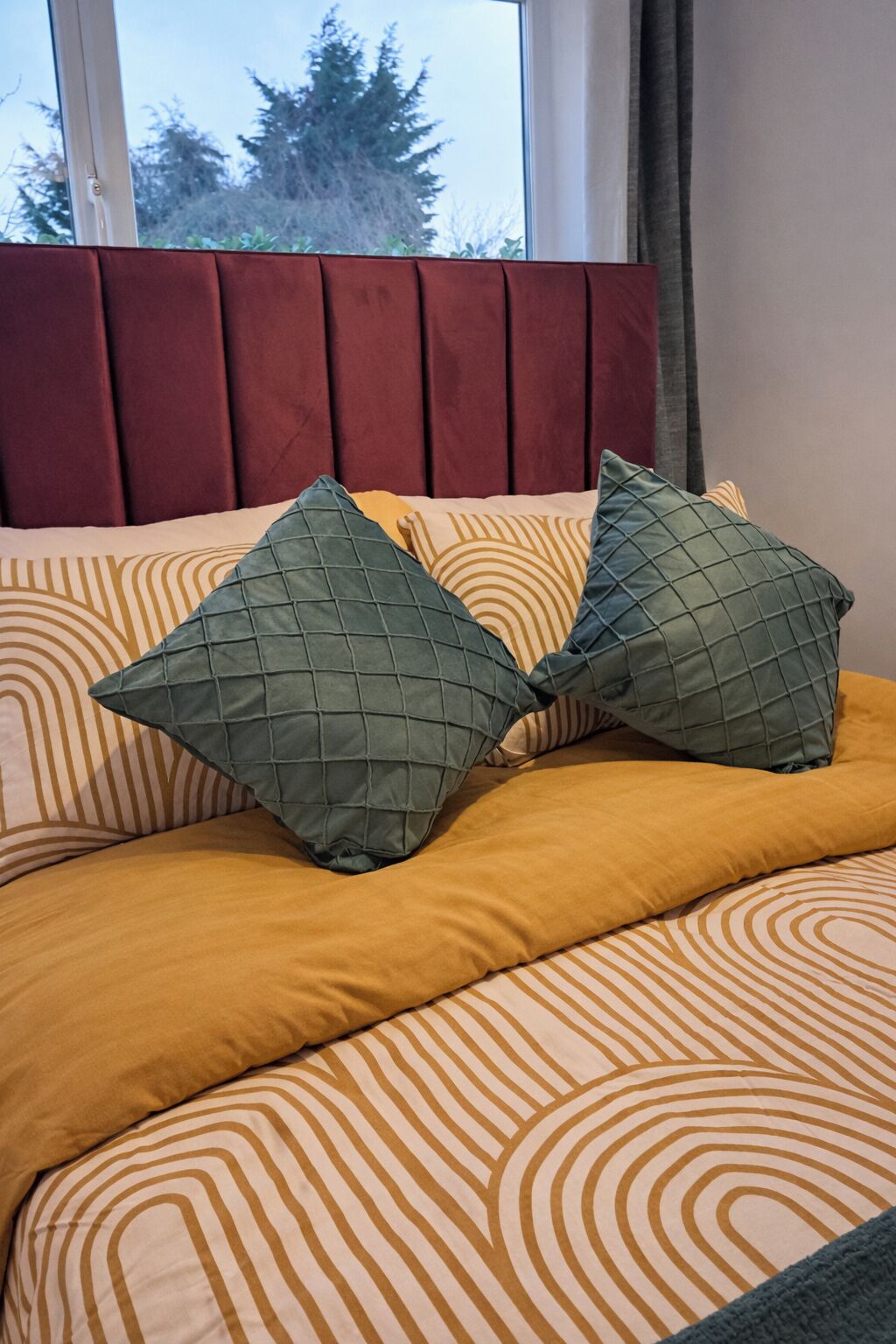 Uma cama com colcha estampada, duas almofadas com padrão acolchoado e cabeceira vermelha.