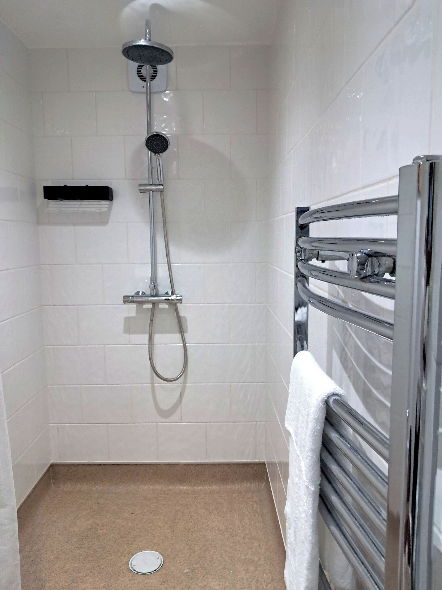 A small, modern shower with a handheld showerhead and a wall-mounted faucet.