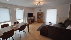A living room with a dining table, chairs, a sofa, a TV, a bookshelf, and a ceiling light fixture. - High-quality, cozy vacation apartment on the first floor - two bedrooms - (Greven)