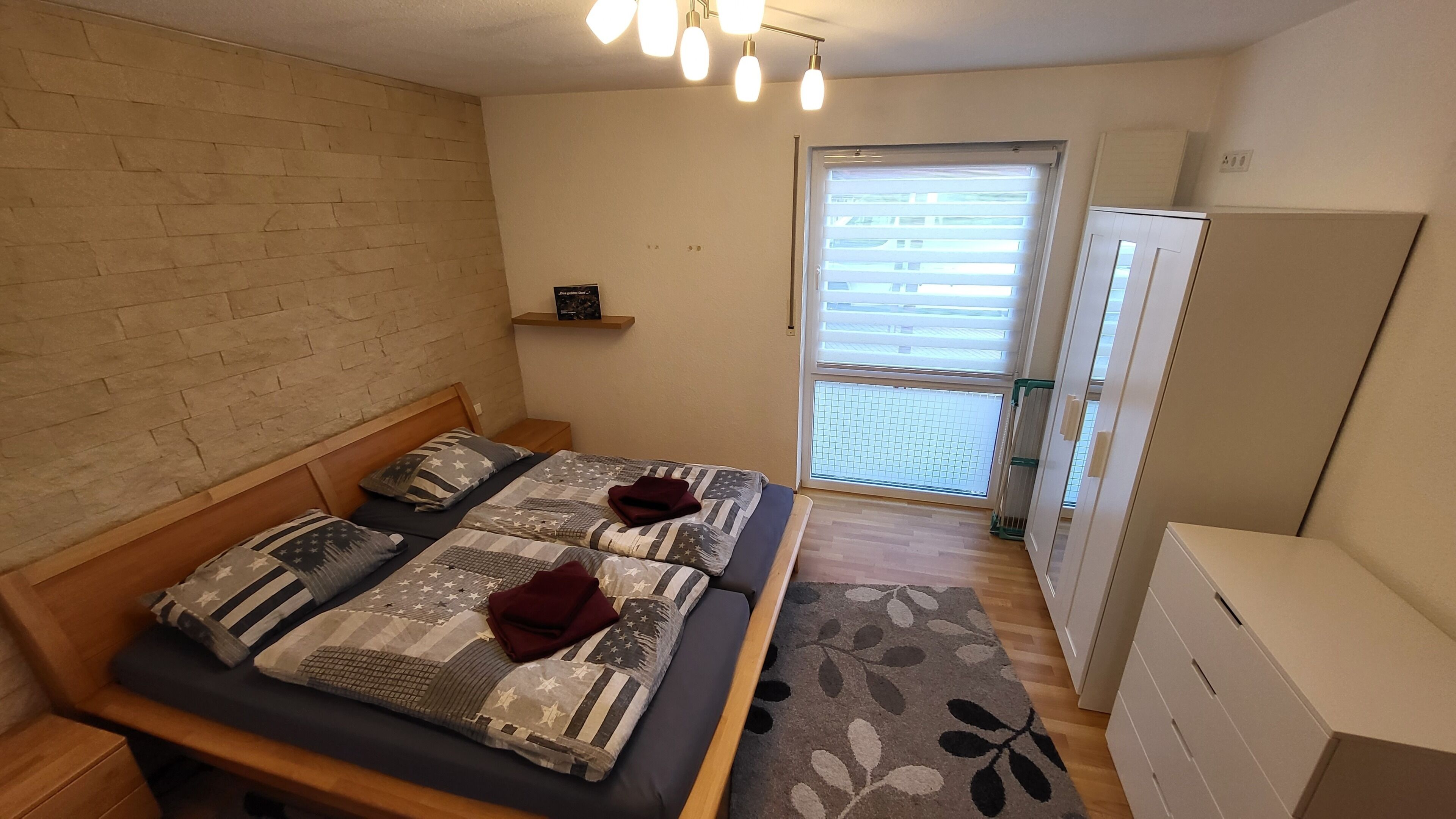 Ein Schlafzimmer mit Bett, Nachttisch, Fenster mit Jalousien, Heizkörper und Kleiderschrank.