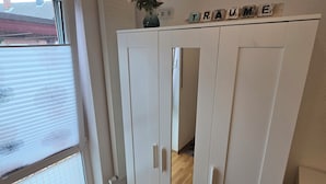 A room with a sliding glass door, a white wardrobe with a mirror, and a small vase with flowers on top. - High-quality, cozy vacation apartment on the first floor - two bedrooms - (Greven)