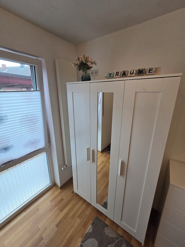 Une pièce dotée d’une porte-fenêtre coulissante, d’une armoire blanche avec un miroir et d’un petit vase orné de fleurs.