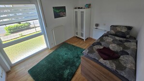 A bedroom with a bed, a radiator, a wardrobe, a green rug, and a window with a view of the outside. - High-quality, cozy vacation apartment on the first floor - two bedrooms - (Greven)