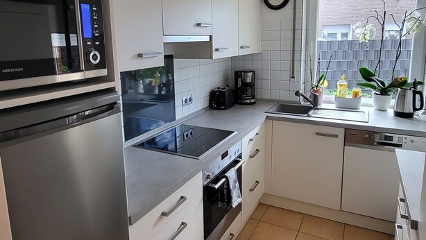 A modern kitchen with white cabinets, stainless steel appliances, and a window with plants. - High-quality, cozy vacation apartment on the first floor - two bedrooms - (Greven)