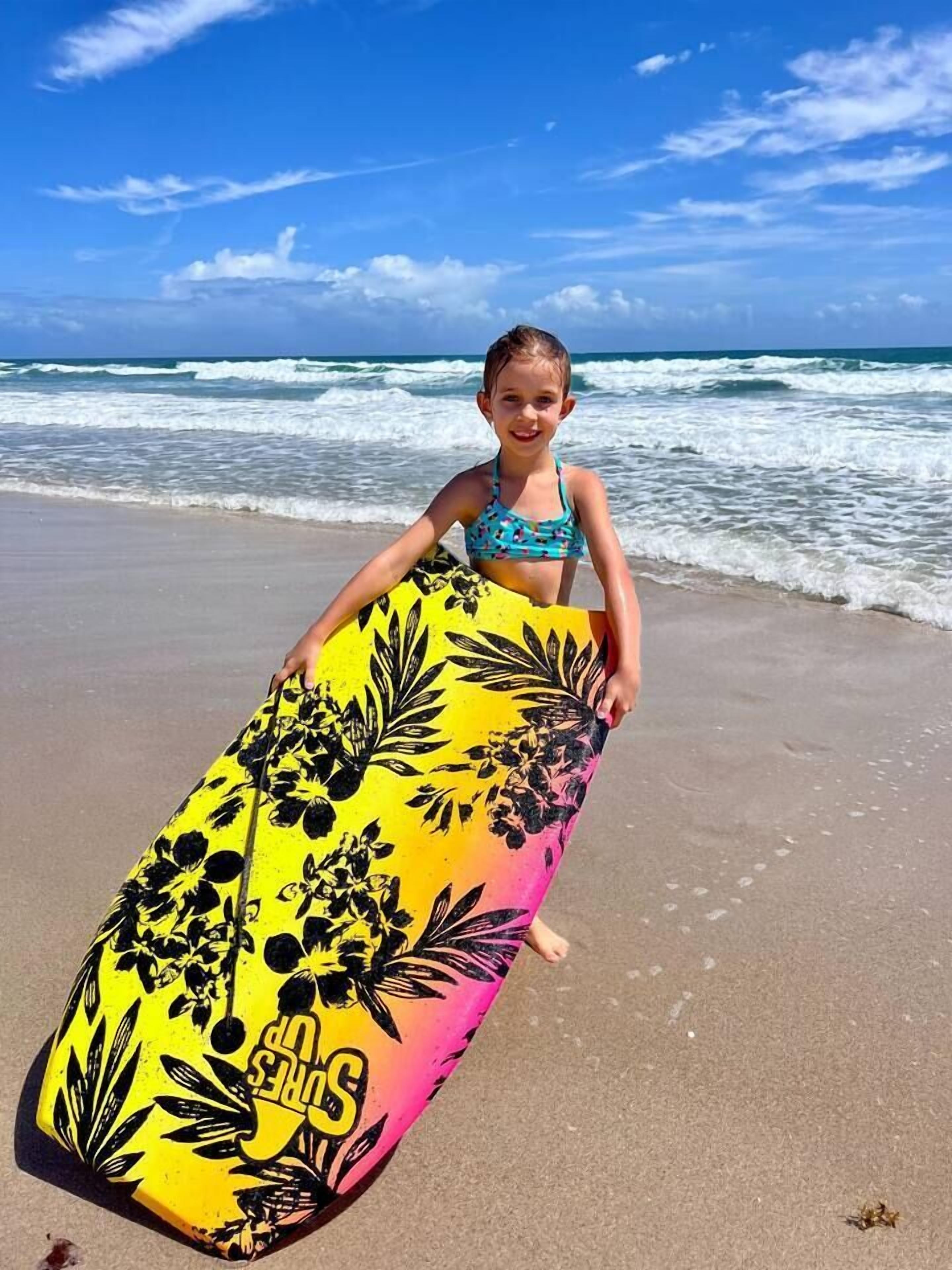 Iemand houdt een surfboard vast op een strand, met golven op de achtergrond.
