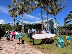 A group of people with surfboards in front of a house with a blue roof and palm trees. - SBH Unit 3 (Fort Pierce)
