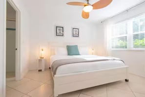 A bedroom with a bed, bedside lamps, a ceiling fan, and a window with blinds.