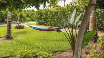 A hammock tied between trees in a well-maintained garden with a lawn and various plants.