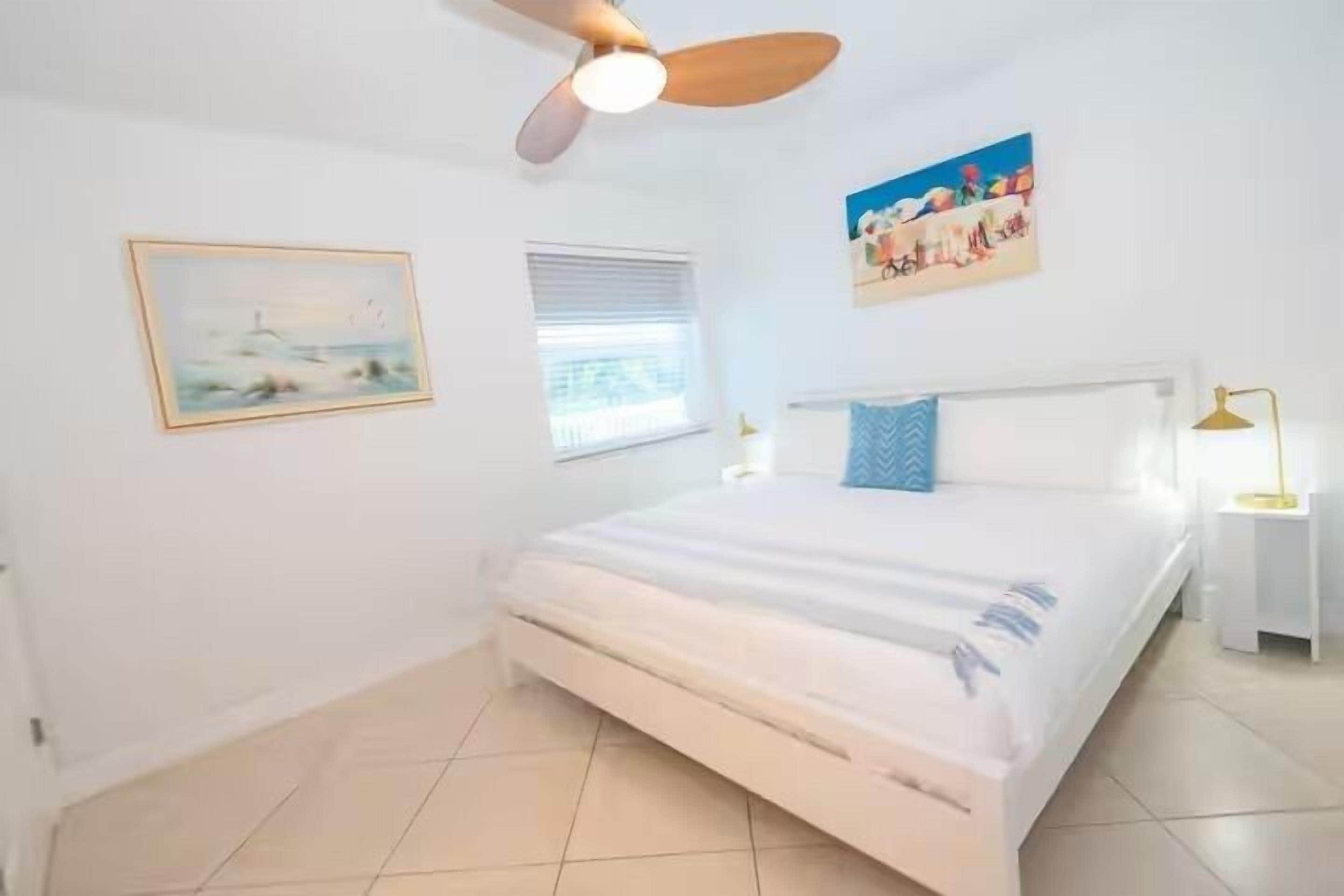 A bedroom with a bed, a ceiling fan, a window, and a nightstand.