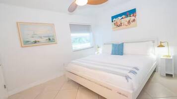 A bedroom with a bed, a ceiling fan, a window, and a nightstand.