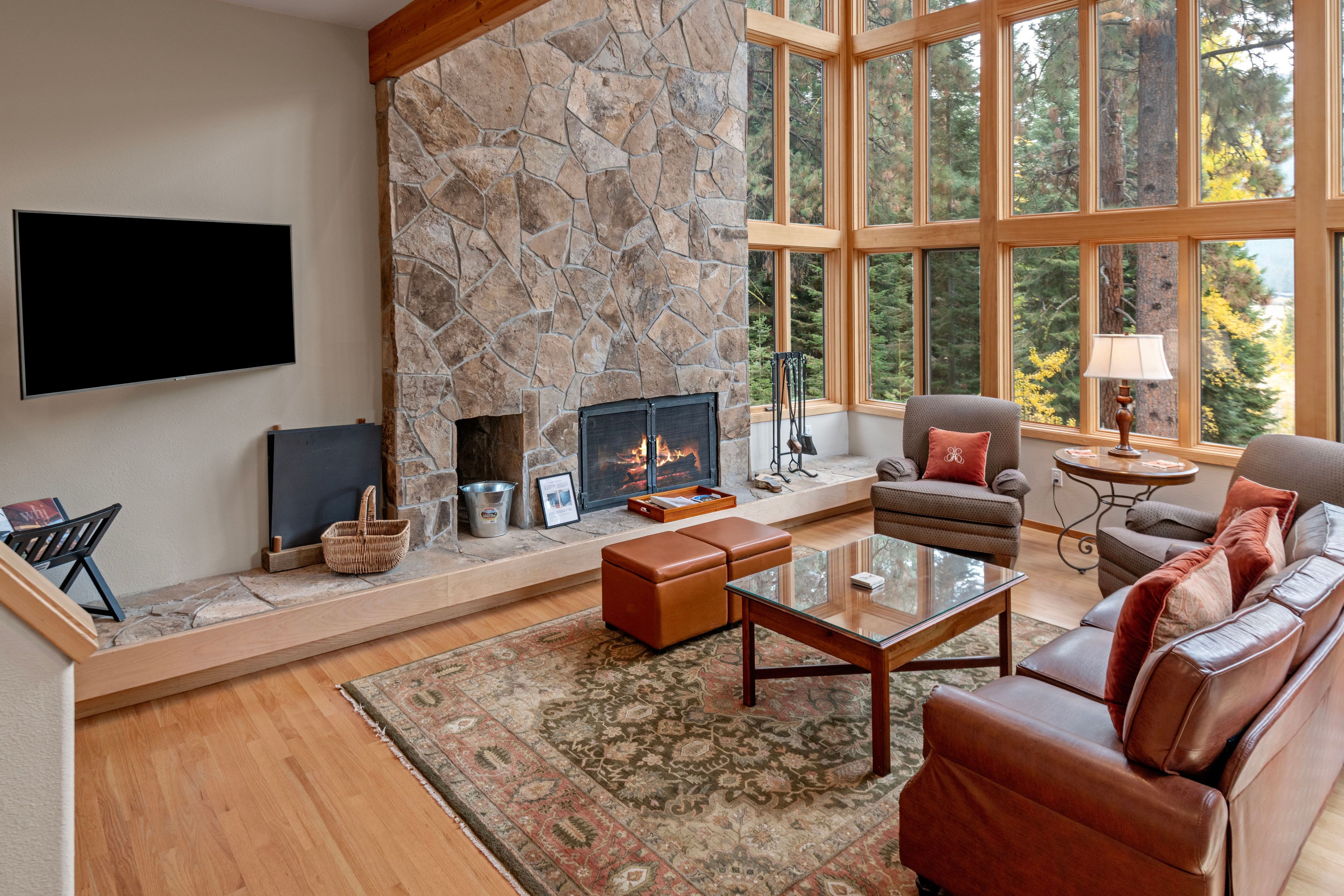 Living room featuring a floor-to-ceiling stone fireplace and large forest-view windows.