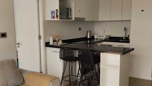 A compact kitchen with a central island, white cabinetry, and a dining area with two chairs. - Comfortable apartment in isla teja sector (Valdivia)