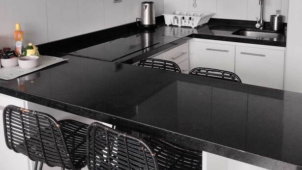 A modern kitchen with a black countertop, white cabinets, and a stainless steel sink. - Comfortable apartment in isla teja sector (Valdivia)