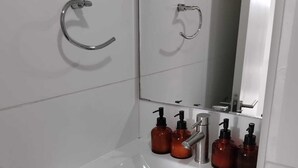 A bathroom with a white sink, chrome faucet, and a mirror above it. There are six brown bottles of soap on the sink. - Comfortable apartment in isla teja sector (Valdivia)