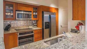A kitchen with wooden cabinets, a stainless steel refrigerator, a microwave, and a granite countertop. - Waterfront condo in beautiful Stuart, Close to Jensen and Stuart beaches. (Stuart)
